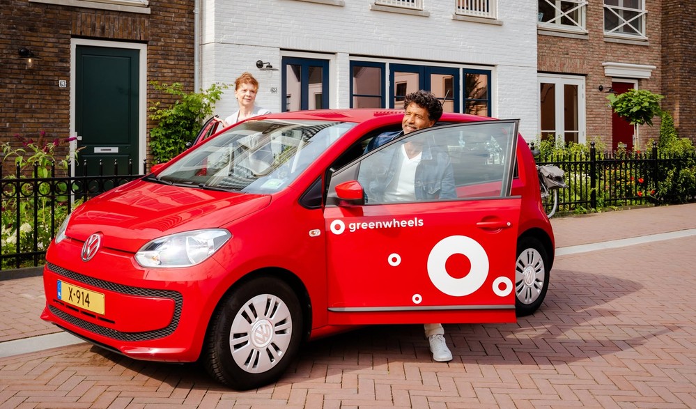 Zwei Menschen, die vor einem Haus in ein rotes Greenwheels-Carsharing-Auto einsteigen