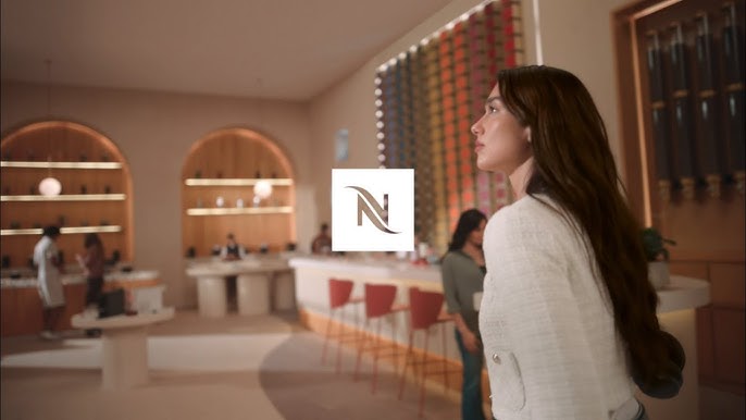 Interior de una boutique Nespresso con una clienta explorando la tienda, de la campaña global Vertuo World con Dua Lipa